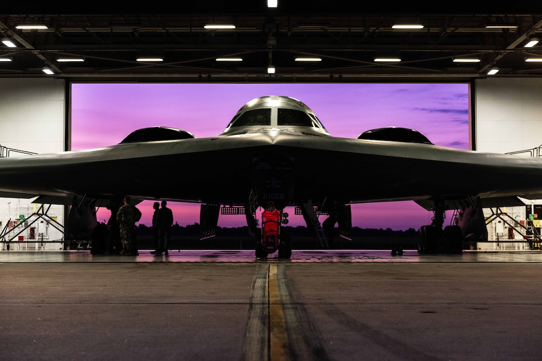 A B-2 Spirit aircraft sits in front of a purple screen a hangar .