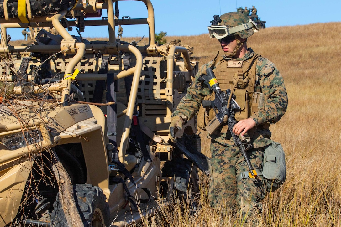 A Marine stands next to a vehicle applying brush.