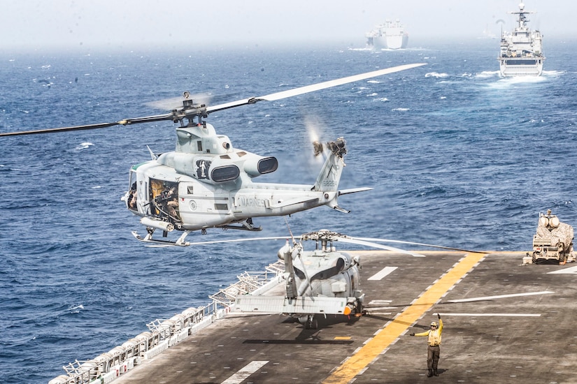 A helicopter takes off as ships sail the sea.