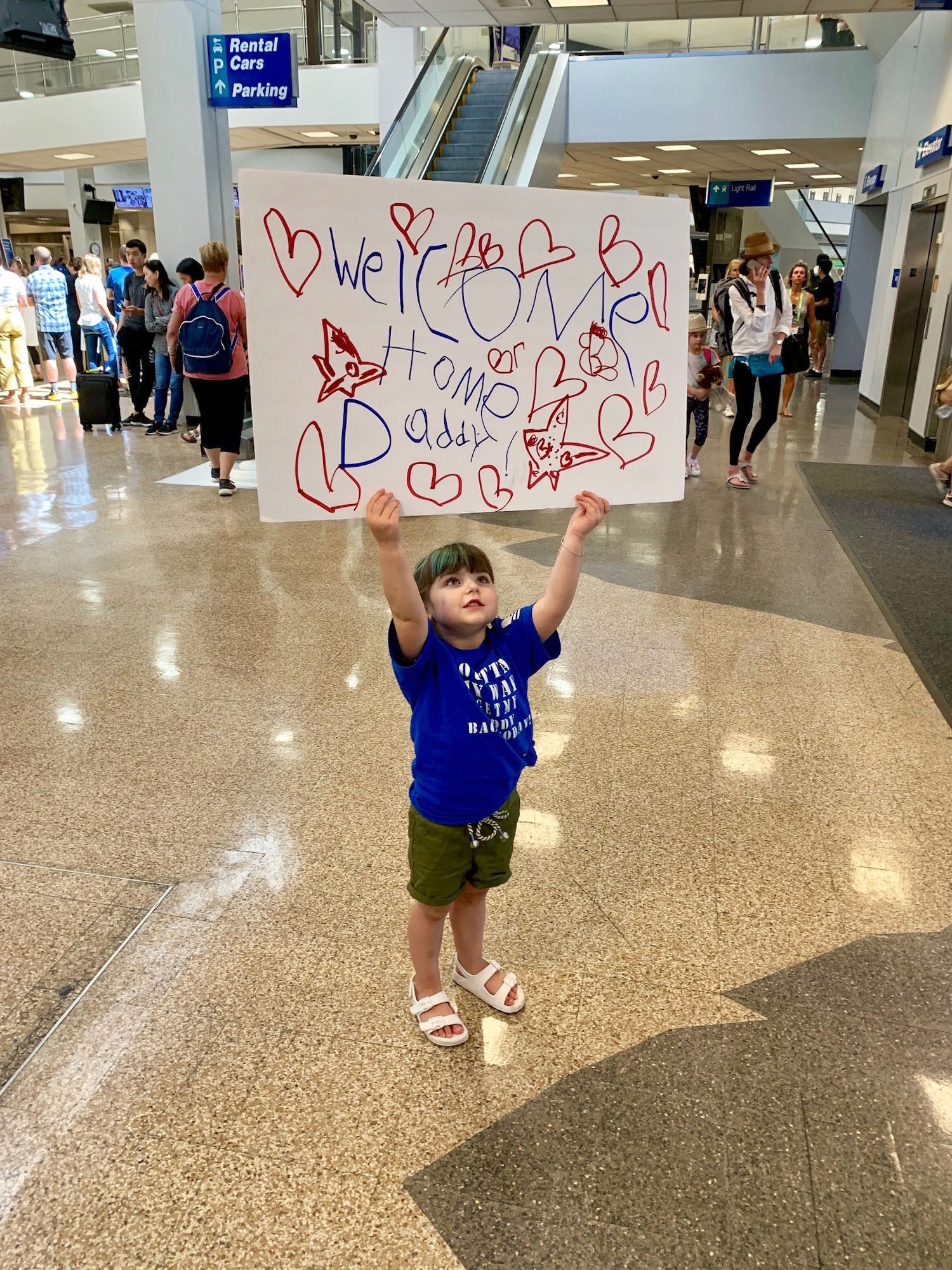 Marley holds up a sign to greet her father, Senior Airman Tyson Kimber, upon his return from a three-month deployment to the United Arab Emirates on July 19.
