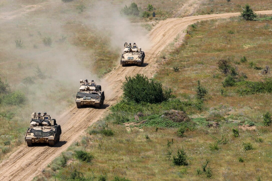 Three military vehicles move on a dirt road.