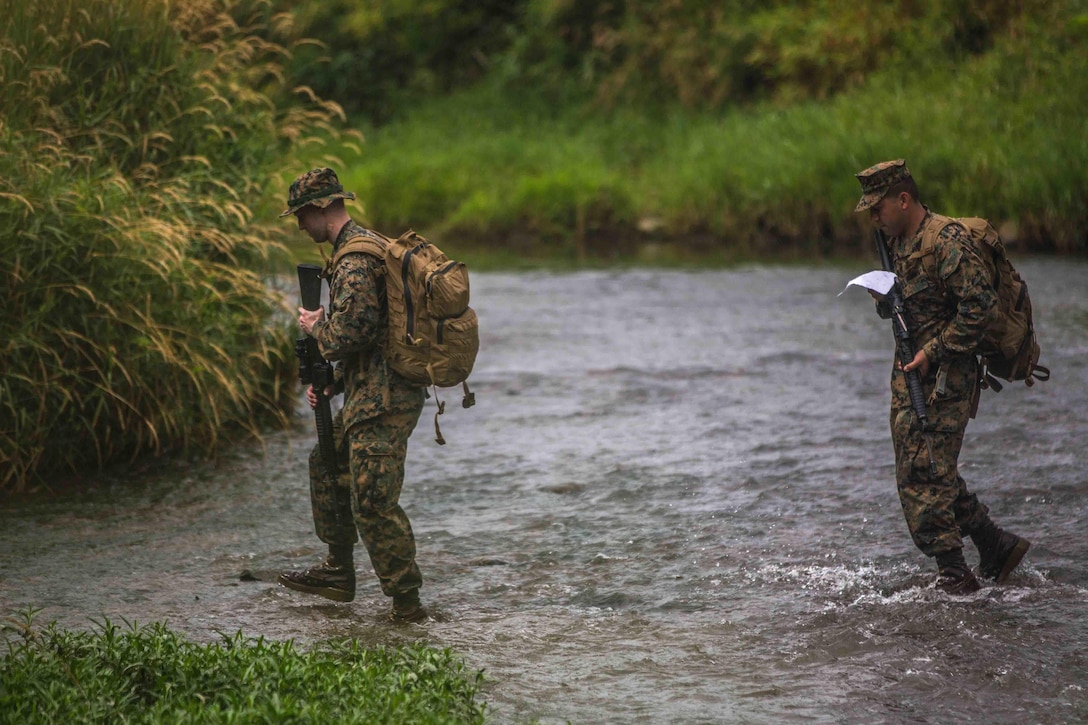 Two Marines walk across a shallow river.