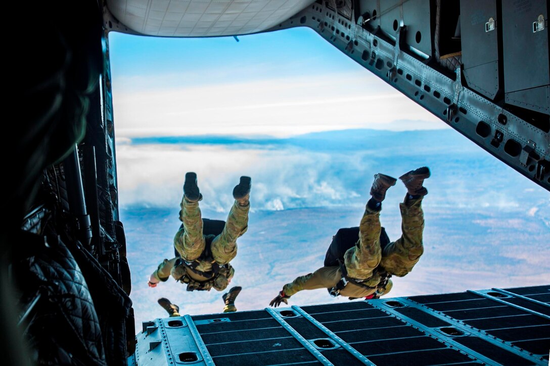 Two people jump out the back of an aircraft into the sky.