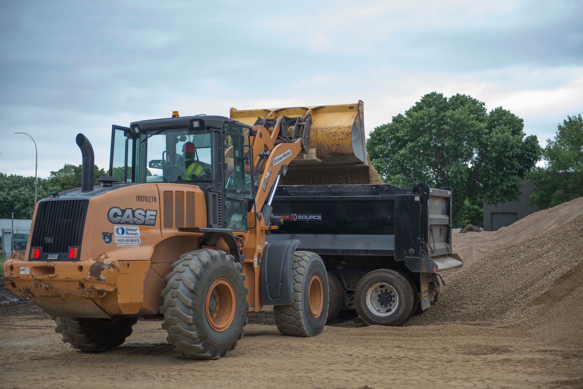 Master Sgt. Johnny Cunningham, 560th RED HORSE Squadron rotational NCO in charge, pours material into a 20-ton dump truck using a front end loader at a construction site on Minneapolis-St. Paul Air Reserve Station, Minn., July 10, 2019.