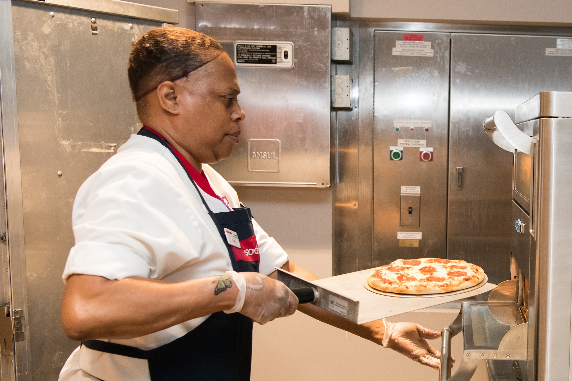 Pamela Marshall, Sodexo cook, pulls a pizza out of the oven June 11, 2019, at the Patterson Dining Facility, Dover Air Force Base, Del. The Slice of Life pizza station offers DFAC patrons fresh-baked personal pan pizzas with traditional toppings, as well as specialty pizzas. (U.S. Air Force photo by Mauricio Campino)