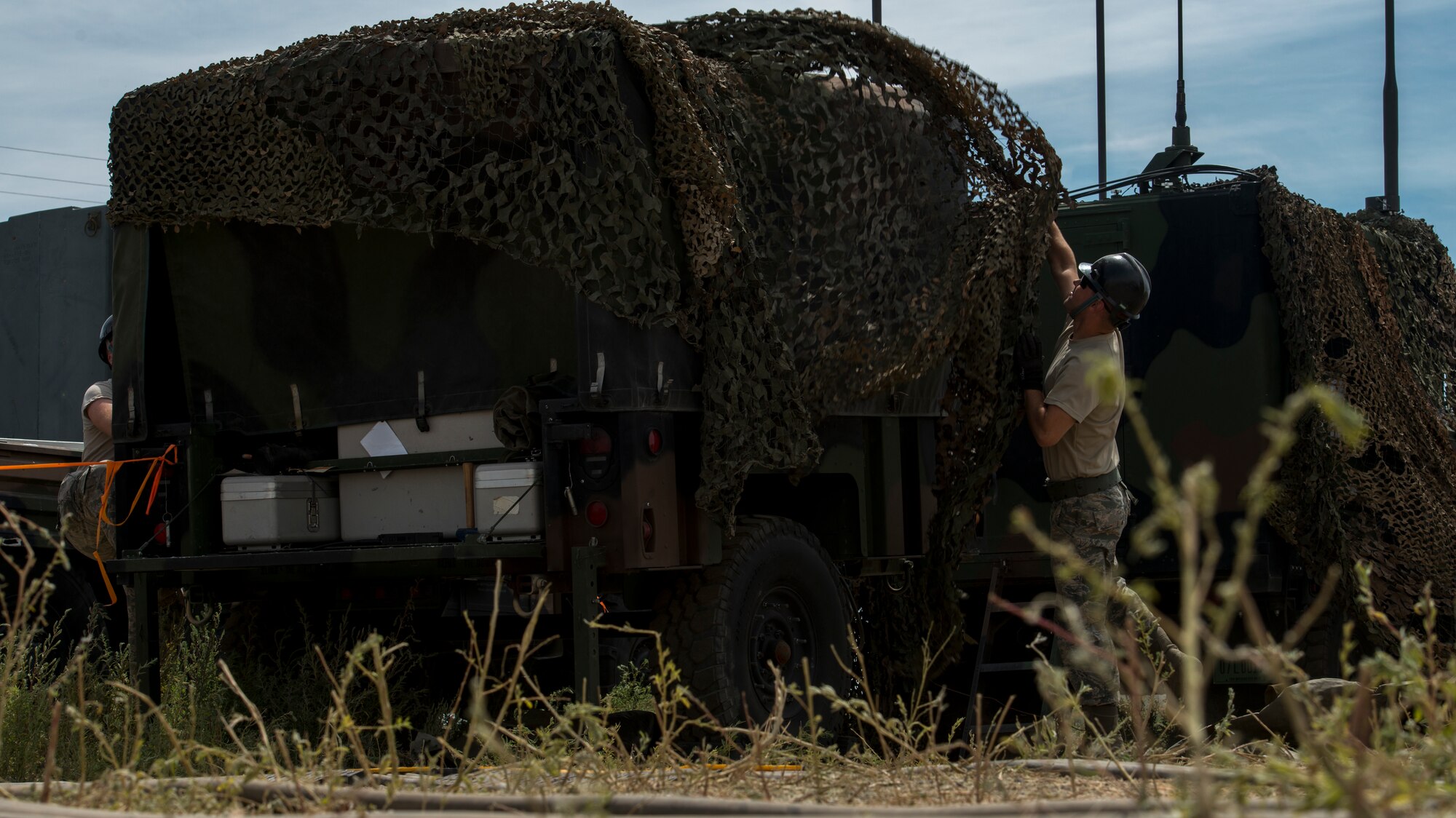 Senior Airman Jordan Jones, 726th Air Control Squadron radio frequency (RF) transmission systems technician, throws a camouflage tarp over a radio unit (RU) July 16, 2019, at Mountain Home Air Force Base, Idaho. Jones worked countless hours with his team to set up RUs and Tropo Satellite Support Radio (TSSRs) for Hardrock exercise 19-2. (U.S. Air Force photo by Senior Airman JaNae Capuno)