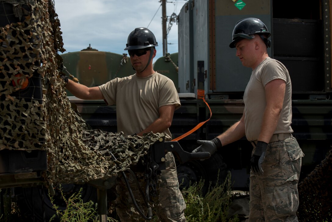 Senior Airman Jordan Jones and Senior Airman Paul Sexner, 726th Air Control Squadron radio frequency (RF) transmission systems technicians, secure a camouflage tarp over a radio unit (RU) July 16, 2019, at Mountain Home Air Force Base, Idaho. Jones worked countless hours with his team to set up RUs and Tropo Satellite Support Radio (TSSRs) for Hardrock exercise 19-2. (U.S. Air Force photo by Senior Airman JaNae Capuno)