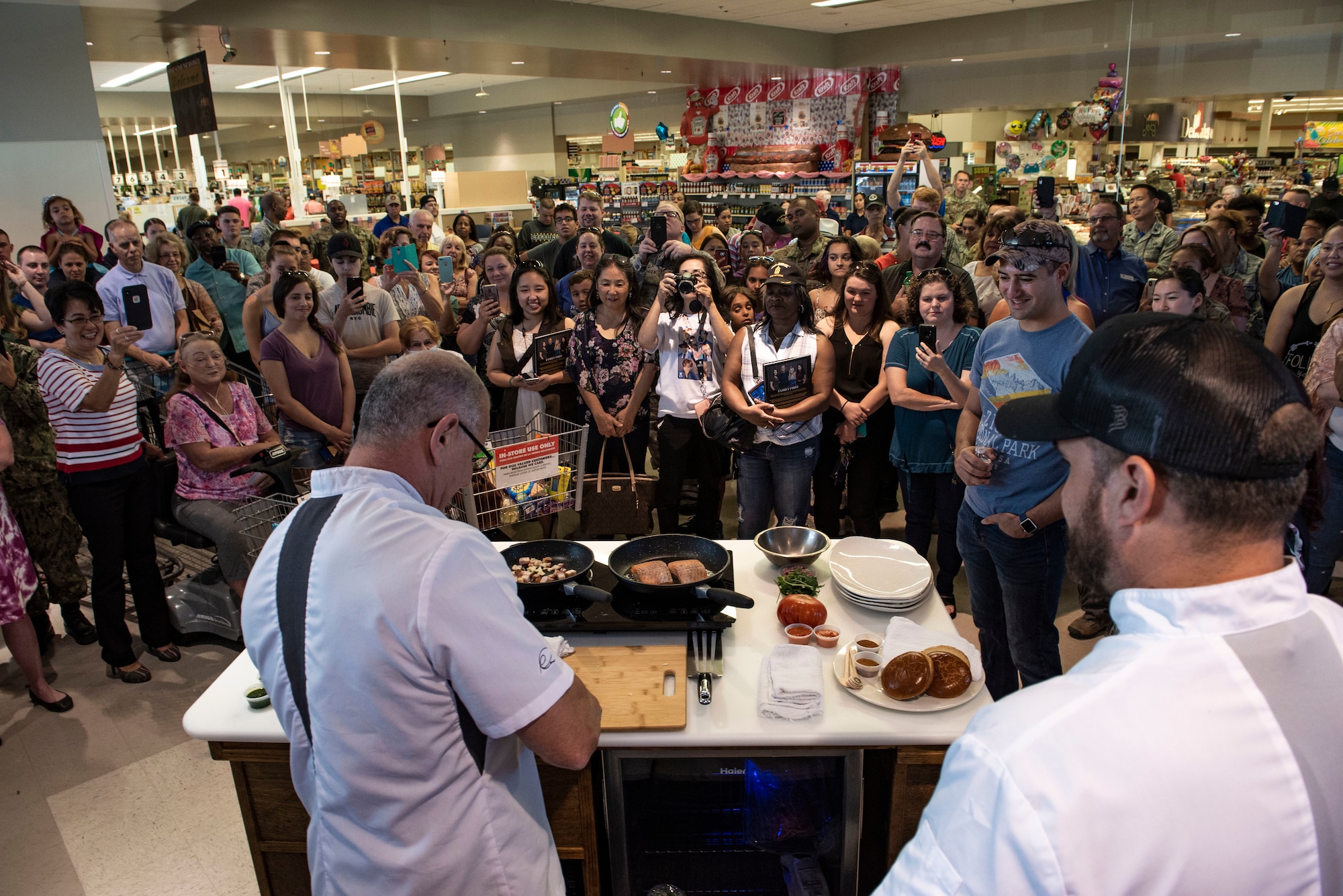 Members of team Nellis look on as celebrity chef Robert Irvine prepares a dish at the Nellis Commissary on Nellis Air Force Base, Nev., July 19, 2019.