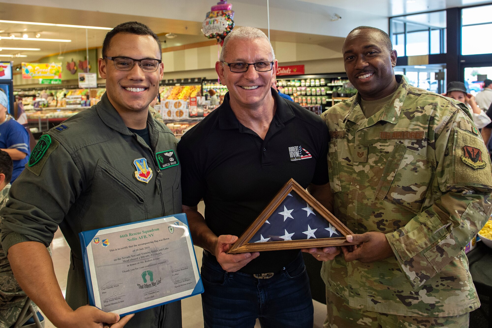 Celebrity Chef Robert Irvine (center) receives an American flag that was flown by the 66th Rescue Squadron on Nellis Air Force Base, Nev., July 19, 2019.