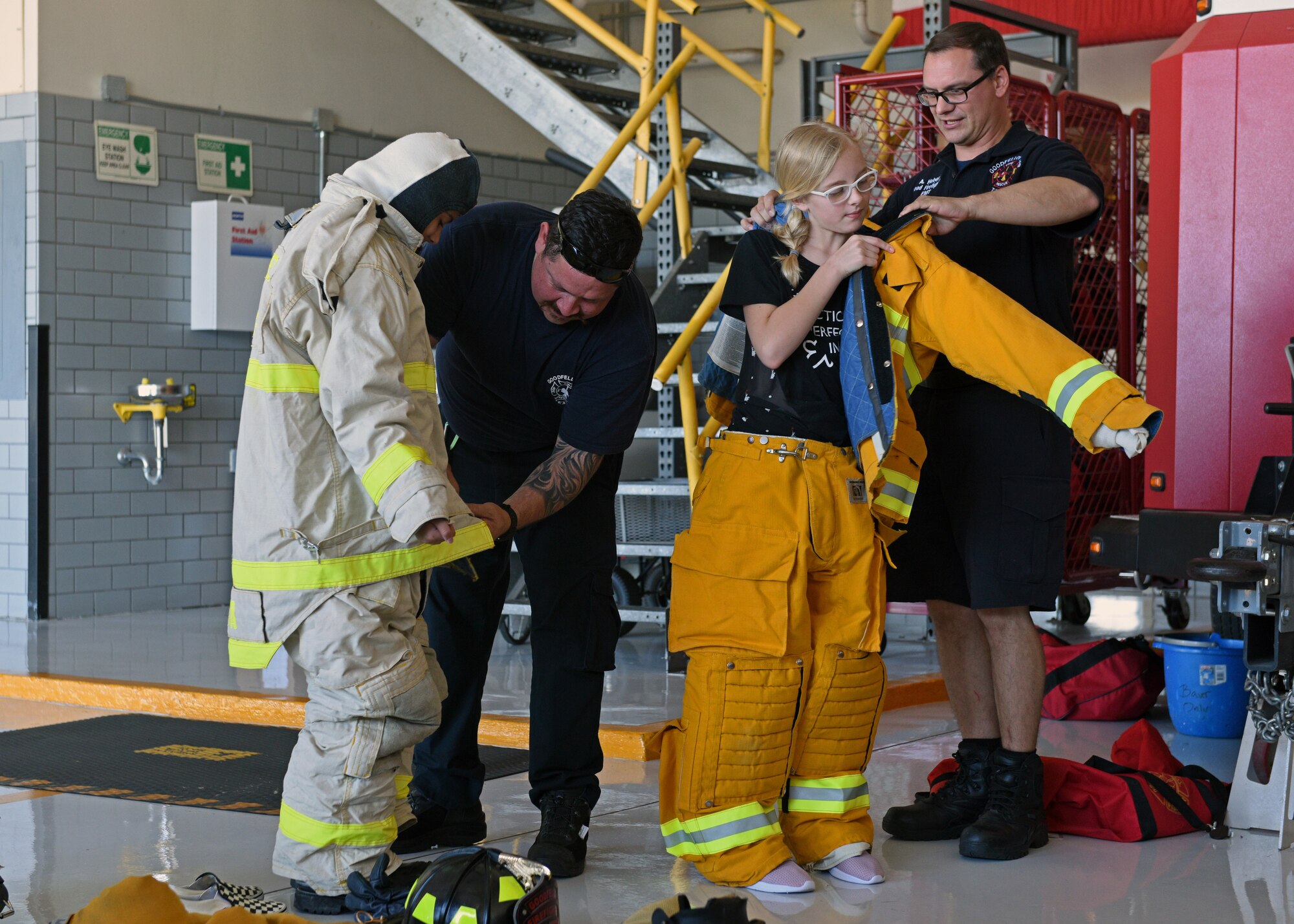 17th Civil Engineering Squadron Firefighters, Lieutenant Roger Abalos and Captain Alan Hebert, assist junior firefighters as they don their protective gear at the Goodfellow Air Force Base Fire Department on Goodfellow Air Force Base, Texas, July 16, 2019. The junior firefighters took turns wearing the firefighter uniforms to get a feel for what firefighters must do to protect themselves before heading out to the scene of a fire. (U.S. Air Force photo by Airman 1st Class Robyn Hunsinger/Released)