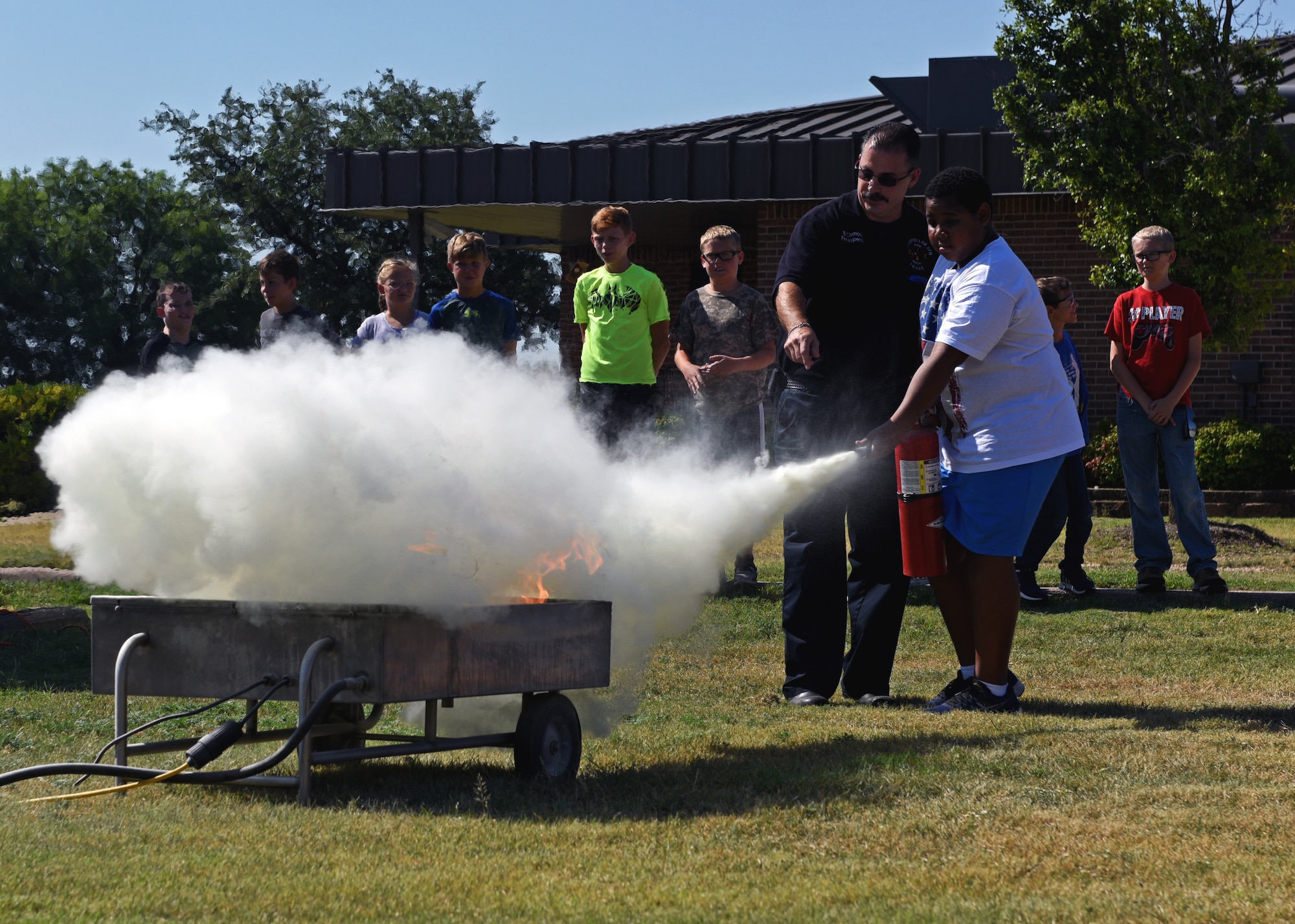 17th Civil Engineering Squadron Fire Inspector, Billy Clemons, directs a junior firefighter as he extinguishes a live fire at the Goodfellow Air Force Base Fire Department on Goodfellow Air Force Base, Texas, July 16, 2019. The firefighters demonstrated to the children the proper way to use a fire extinguisher. (U.S. Air Force photo by Airman 1st Class Robyn Hunsinger/Released)