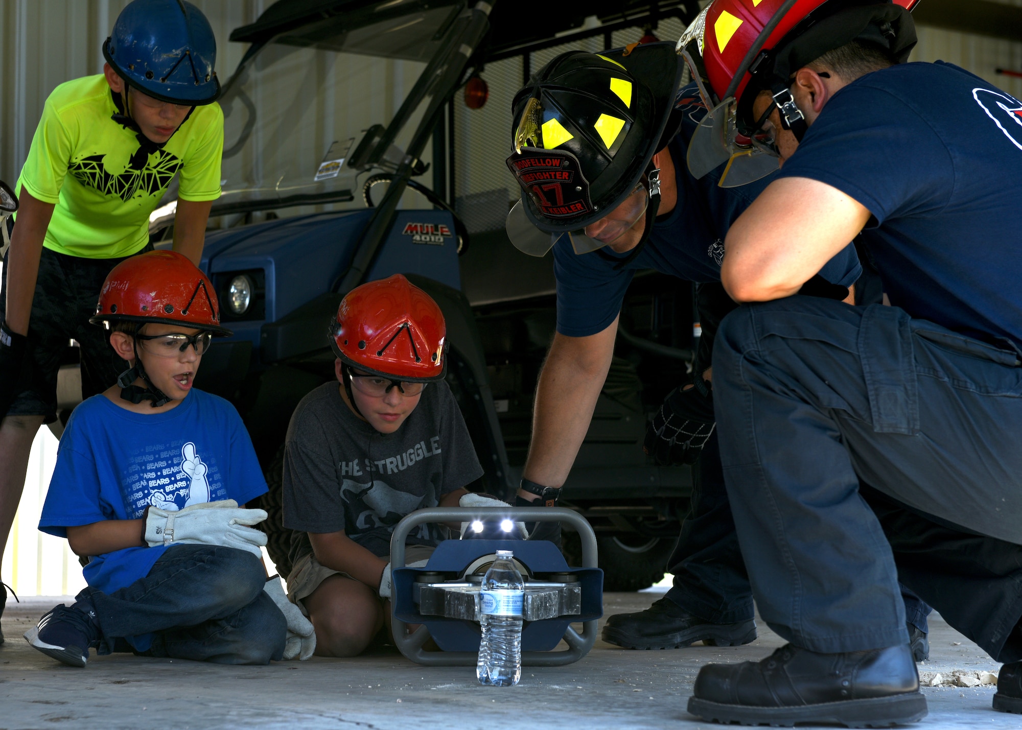 17th Civil Engineering Squadron Firefighters, Bradley Keibler and Captain Daniel Chapa, assist a junior firefighter during a drill in which the children were meant to grip the water bottle with the rescue tools to see how they function at the Goodfellow Air Force Base Fire Department on Goodfellow Air Force Base, Texas, July 16, 2019. They learned just how precise firefighters must be in order to use these tools in emergency situations. (U.S. Air Force photo by Airman 1st Class Robyn Hunsinger/Released)