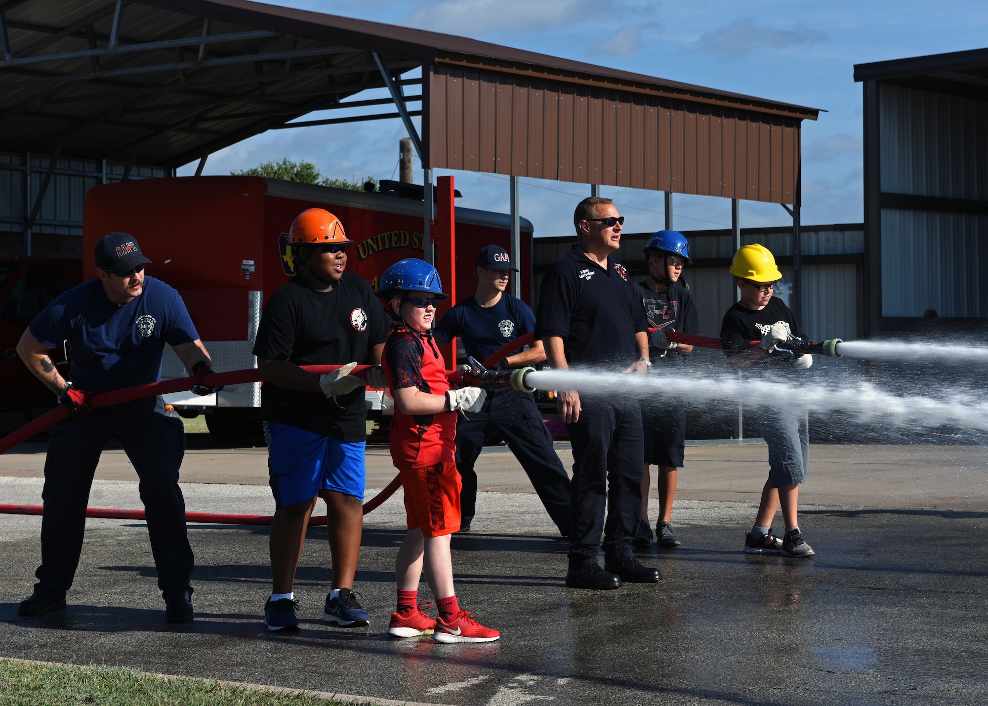 Firefighters from the 17th Civil Engineering Squadron train junior firefighters how to properly operate a fire hose at the Goodfellow Air Force Base Fire Department on Goodfellow Air Force Base, Texas, July 17, 2019. The junior firefighters completed a drill in which they learned how to correctly carry the hose and spray water to knock road cones over. (U.S. Air Force photo by Airman 1st Class Robyn Hunsinger/Released)