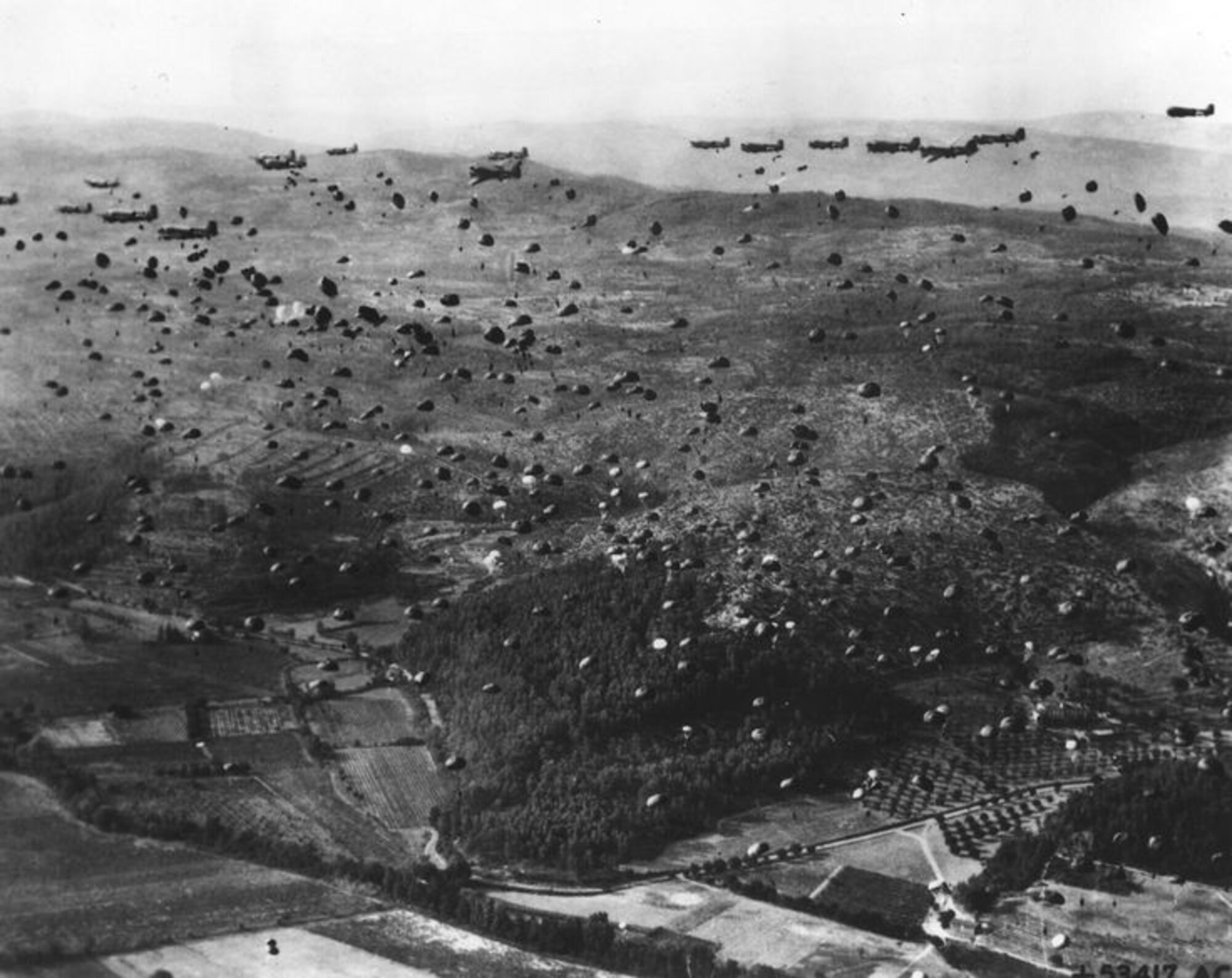 Paratroopers from the 1st Airborne Task Force dropping from Dakotas on one of the three RUGBY drop zones inland while Allied naval landings attacked from the coast seen towards top of picture.