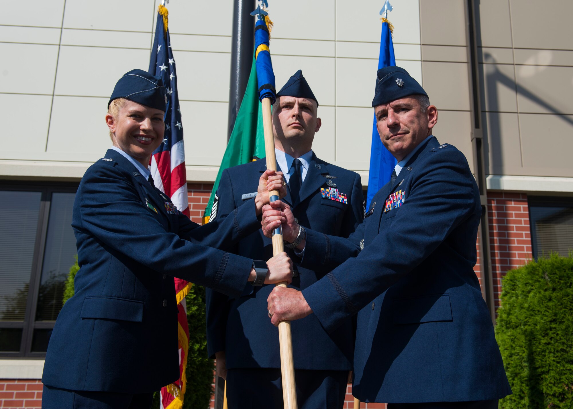 U.S. Air Force Lt. Col. Heather Nelson, 92nd Medical Group commander, passes the new 92nd Health Care Operations Squadron guidon to Lt. Col. Michael McCarthy, 92nd HCOS commander, during a re-designation ceremony at Fairchild Air Force Base, Washington, July 19, 2019. The purpose of the medical re-designation is to better focus resources to promote readiness and ensure the retirees and beneficiaries receive their health care benefits. (U.S. Air Force photo by Airman 1st Class Lawrence Sena)