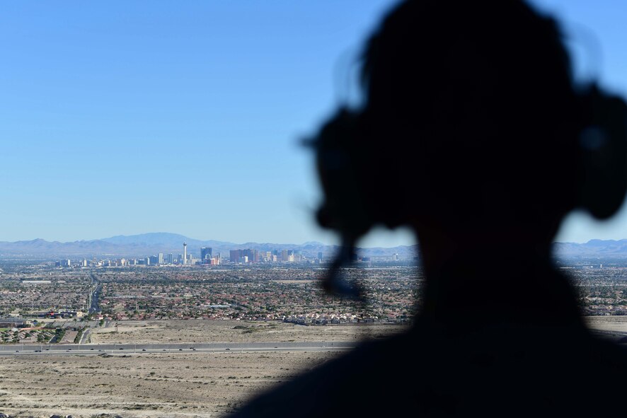 Airman 1st Class William Rosado, 432nd Wing/432nd Air Expeditionary Wing photojournalist, looks out at the Las Vegas skyline from a 66th Rescue Squadron HH-60G Pave Hawk, July 15, 2019. Aircrew with the 66th RS conducted training exercises on the Nevada Test and Training Range and integrated with MQ-9 Reaper aircrew to document the Reaper in flight. (U.S. Air Force photo by Senior Airman Haley Stevens)