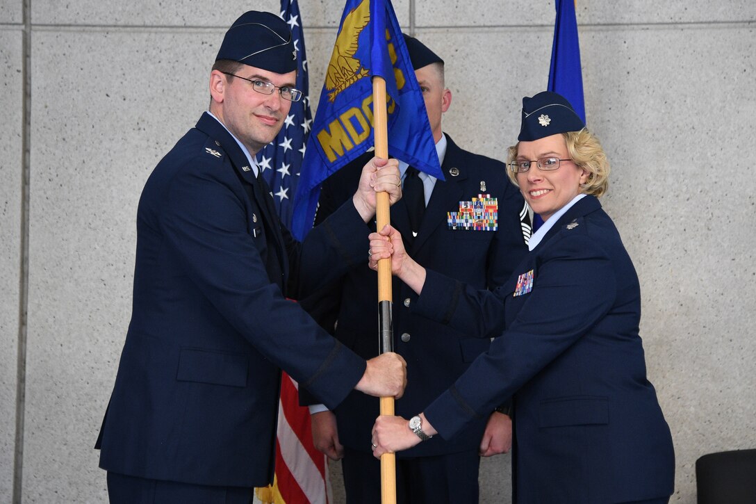 Col. Mark Cleveland, 75th Medical Group commander, passes  the guidon to Lt. Col. Stephanie Ellenburg as Ellenburg assumes command of 75th Medical Operations Squadron during a change of command ceremony July 16, 2019, at Hill Air Force Base, Utah. Following the change of command, the 75th Medical Operations Squadron was inactivated and redesignated as the 75th Health Care Operations Squadron. The change is part of an Air Force initiative to improve patient care and military readiness. (U.S. Air Force photo by R. Nial Bradshaw)