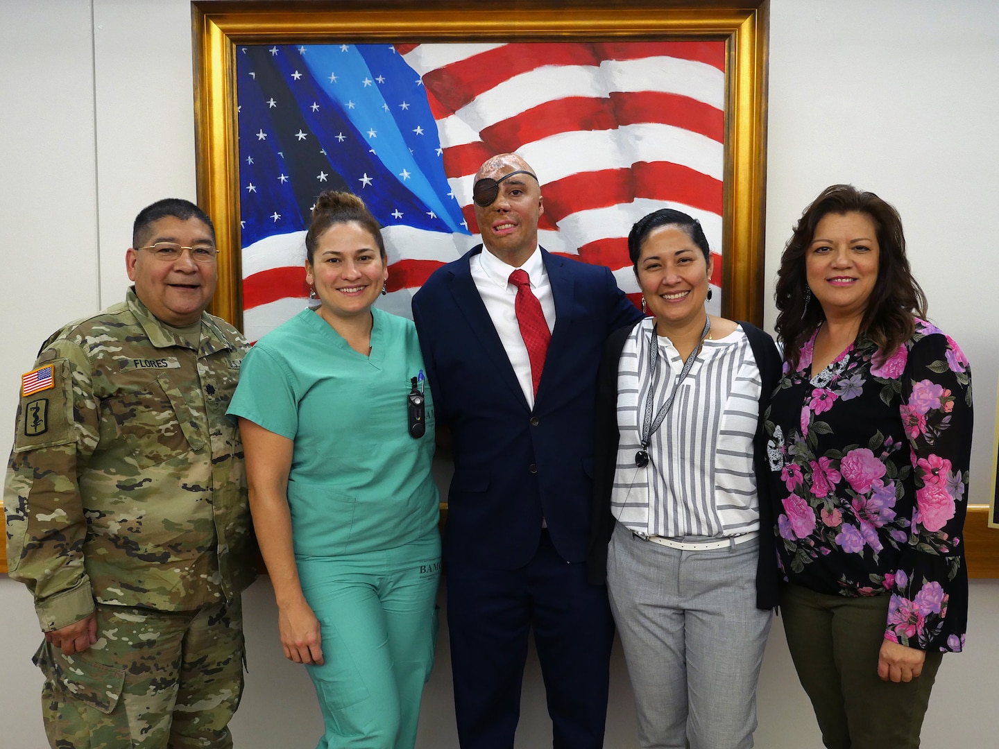 Retired Sgt. Mario Lopez poses for a photo with Brooke Army Medical Center staff members after his painting of the American flag is unveiled in the Medical Mall of the hospital at Joint Base San Antonio-Fort Sam Houston. Lopez, a former BAMC patient who was severely injured in an IED attack in Afghanistan in 2008, learned to use painting therapeutically to help him overcome an array of challenges he has faced over the past decade. The painting was donated to BAMC by former United Nations Ambassador Warren W. Tichenor.