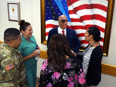 Retired Sgt. Mario Lopez talks with Brooke Army Medical Center staff members after his painting of the American flag is unveiled in the Medical Mall of the hospital at Joint Base San Antonio-Fort Sam Houston. Lopez, a former BAMC patient who was severely injured in an IED attack in Afghanistan in 2008, learned to use painting therapeutically to help him overcome an array of challenges he has faced over the past decade. The painting was donated to BAMC by former United Nations Ambassador Warren W. Tichenor.