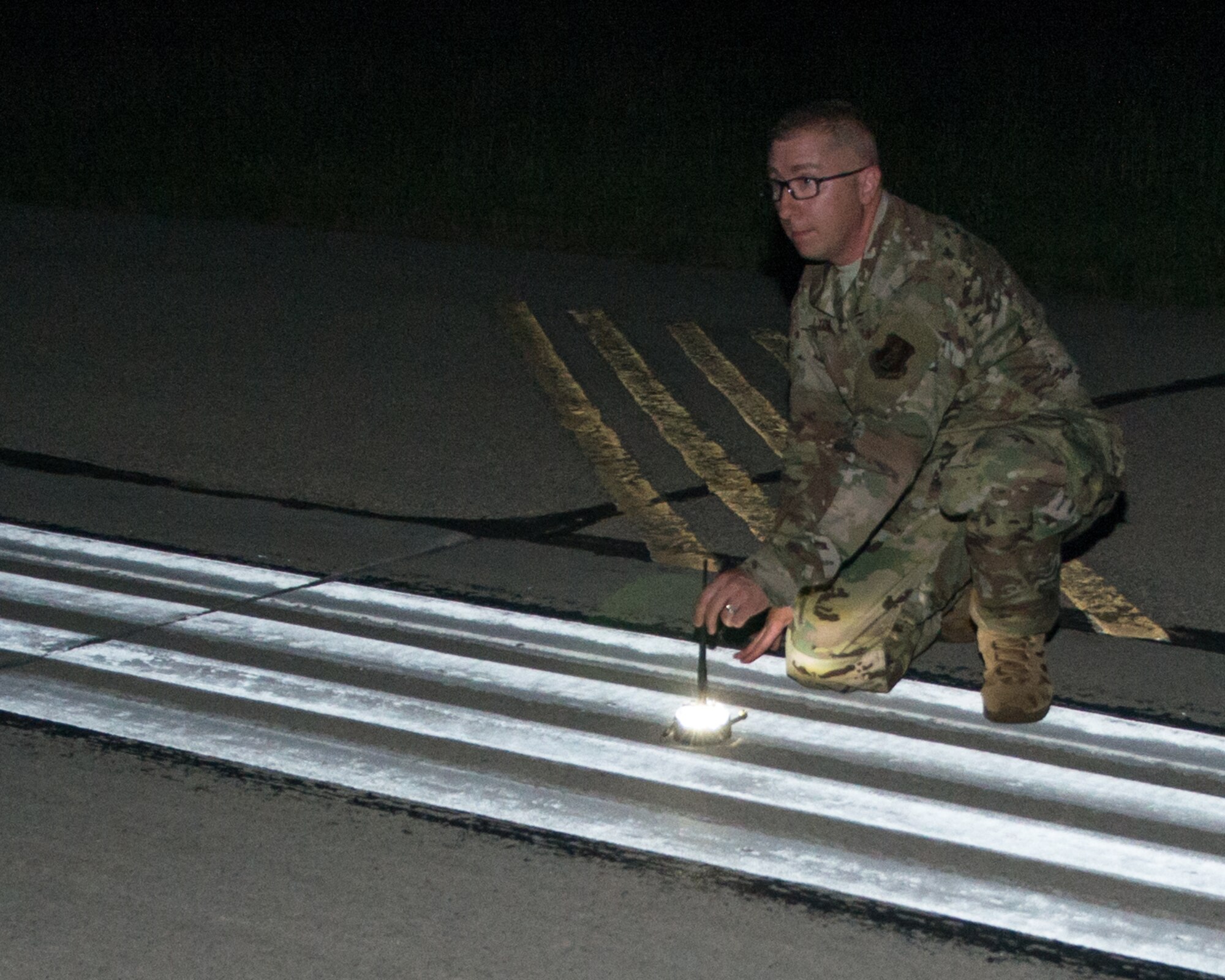 An Airman sets out a Phantom Light on the side of a dark runway.