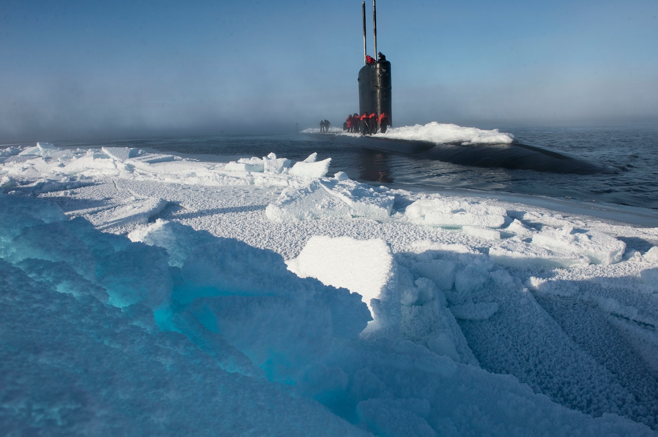 A submarine is surfaced near a large sheet of ice. Snow is piled up on top of the submarine.