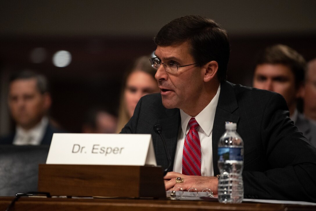 Man seated at a table speaks into a small microphone.