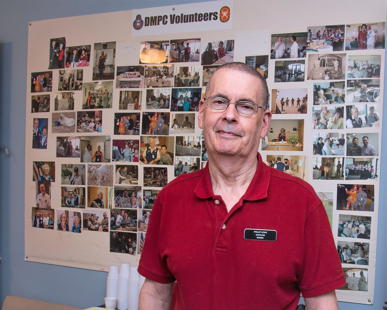 Phil Lewis, Brooke Army Medical Center volunteer since 1996, stands in front of a photo collage of the Department of Ministry & Pastoral Care volunteer office April 16.