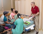 Phillip Lewis (right), on-call chaplain and post anesthesia care unit volunteer, talks with a family in the Post Anesthesia Care Unit at Brooke Army Medical Center, while Air Force Maj. Katherine M. Slogic, pediatric anesthesiologist, listens to the patient’s lungs April 16.