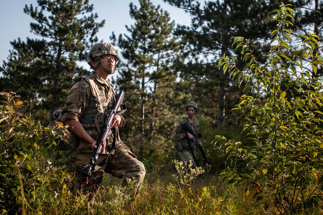 A soldier patrols a wooded area.