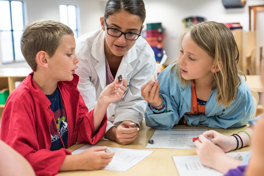 Kaden, 9, left, and Mackenzie, 9, compare rocks while Jaqueline Sanchez, science camp instructor, supervises during the Air Force Science Specialty Camp at the Child Development Center at Schriever Air Force Base, Colorado, July 22, 2019. During this portion of the science camp, children categorized rocks according to a variety of observable properties. (U.S. Air Force photo by 2nd Lt. Idalí Beltré Acevedo)