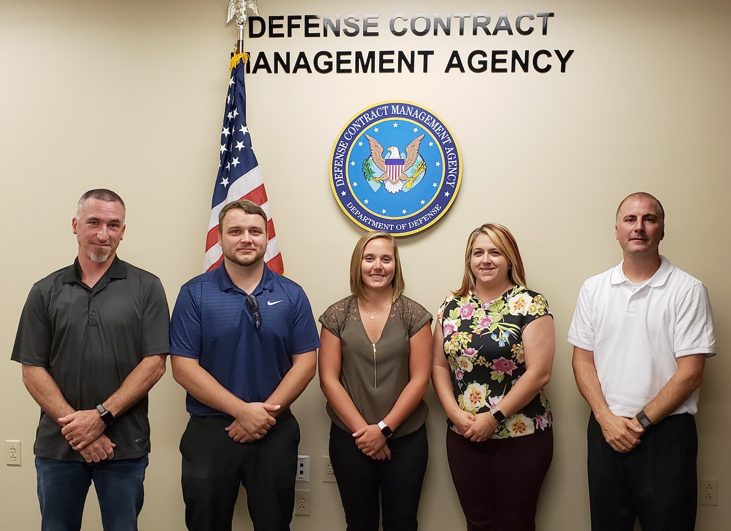 Group photo of male and female employees in front of the American flag and the DCMA seal