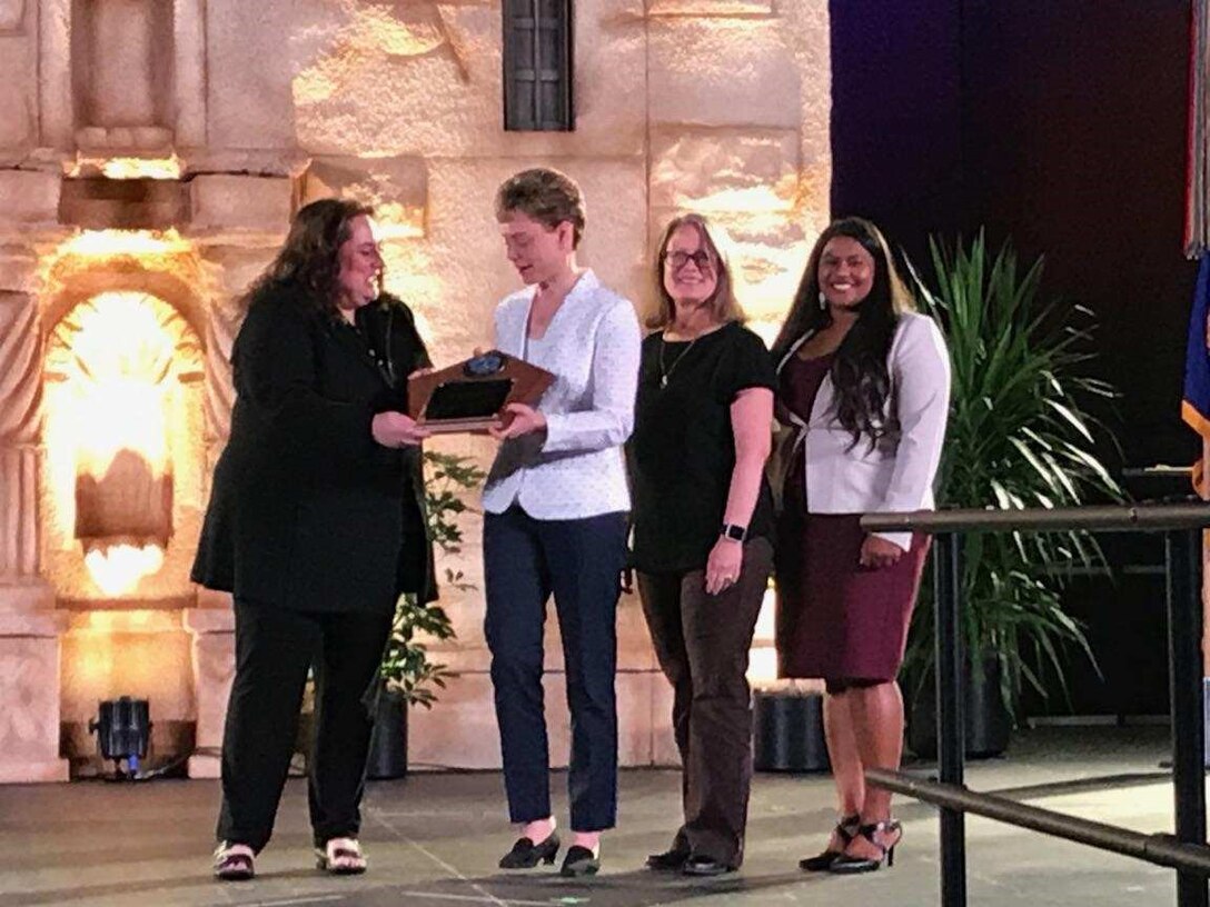 four individuals stand in from of mock up of Alamo and accept award