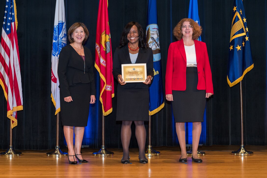 3 individuals pose with one in center holding diploma