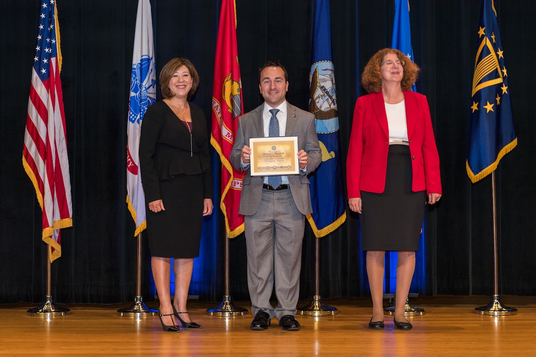 3 individuals pose with one in center holding diploma