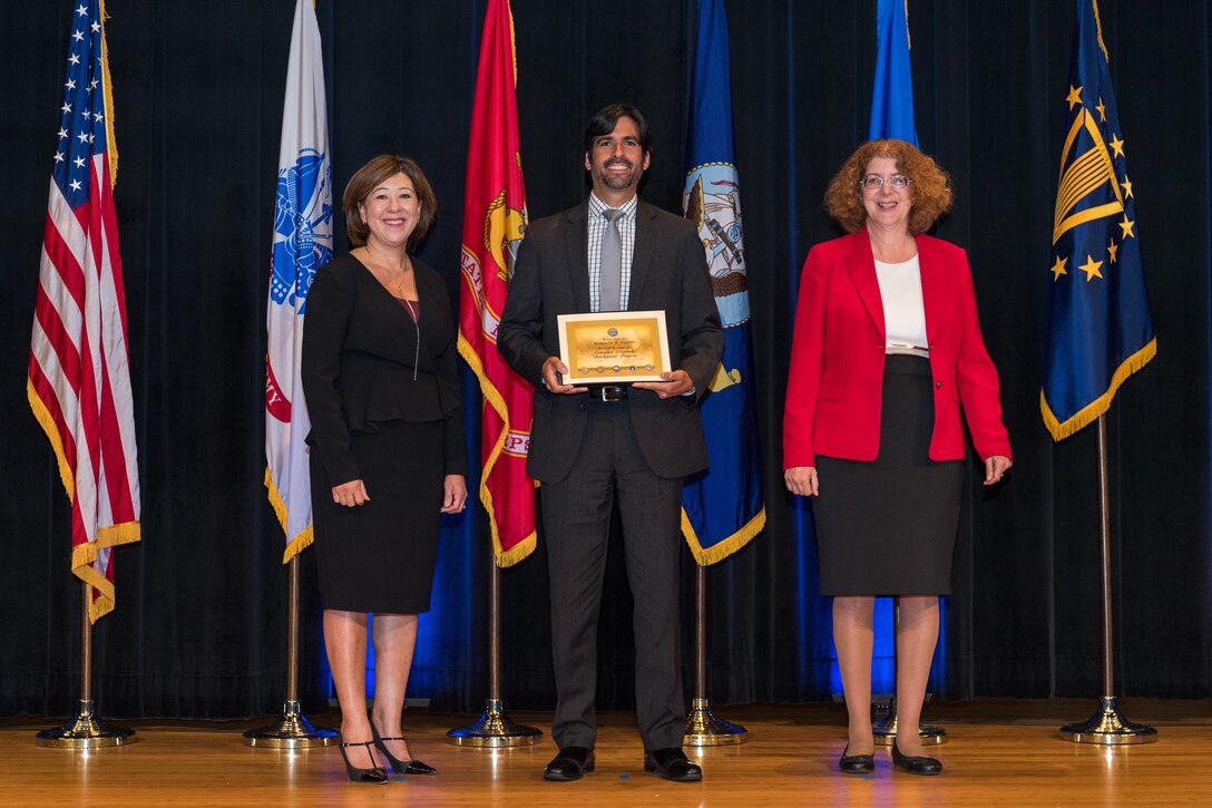 3 individuals pose with one in center holding diploma