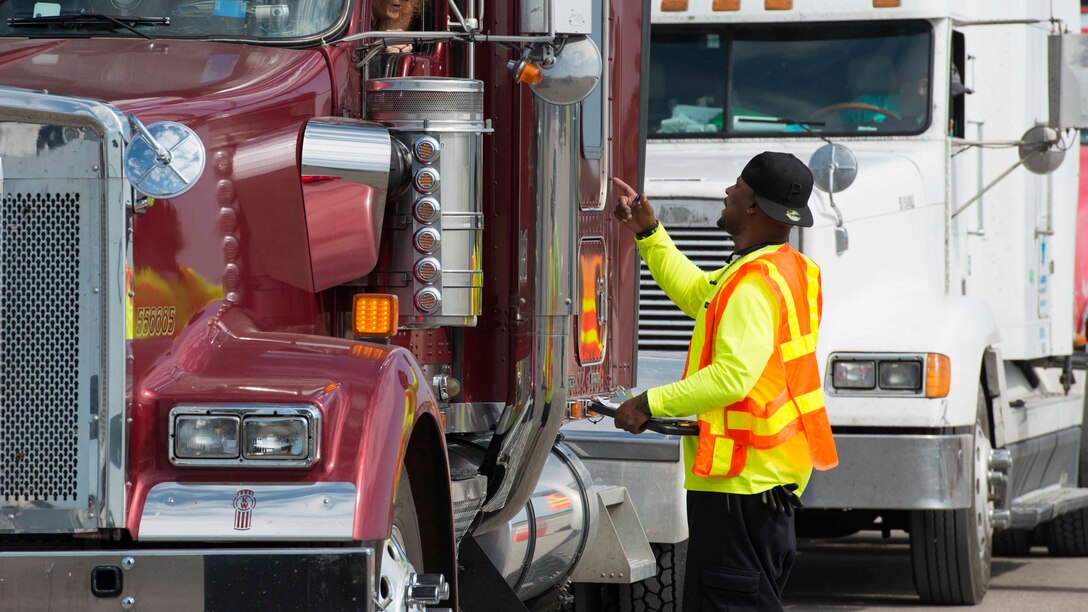 Mario Johnson, wearing a reflective vest and standing beside a truck, speaks to a truck driver