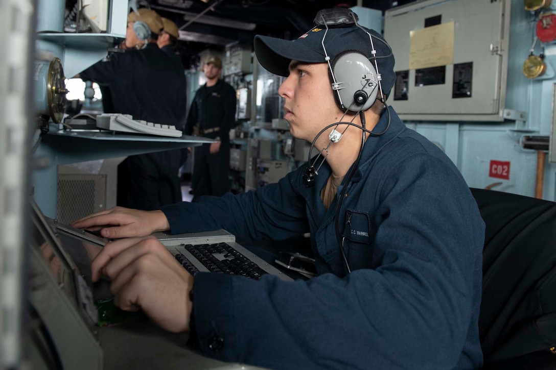 Sailor seated at a console stands watch.