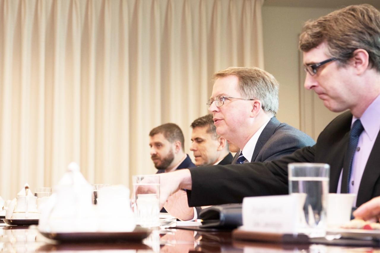 Men seated at meeting table.