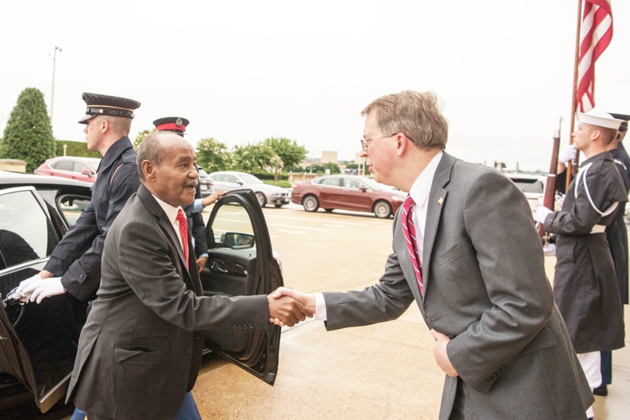 Two men shake hands as one emerges from a car.