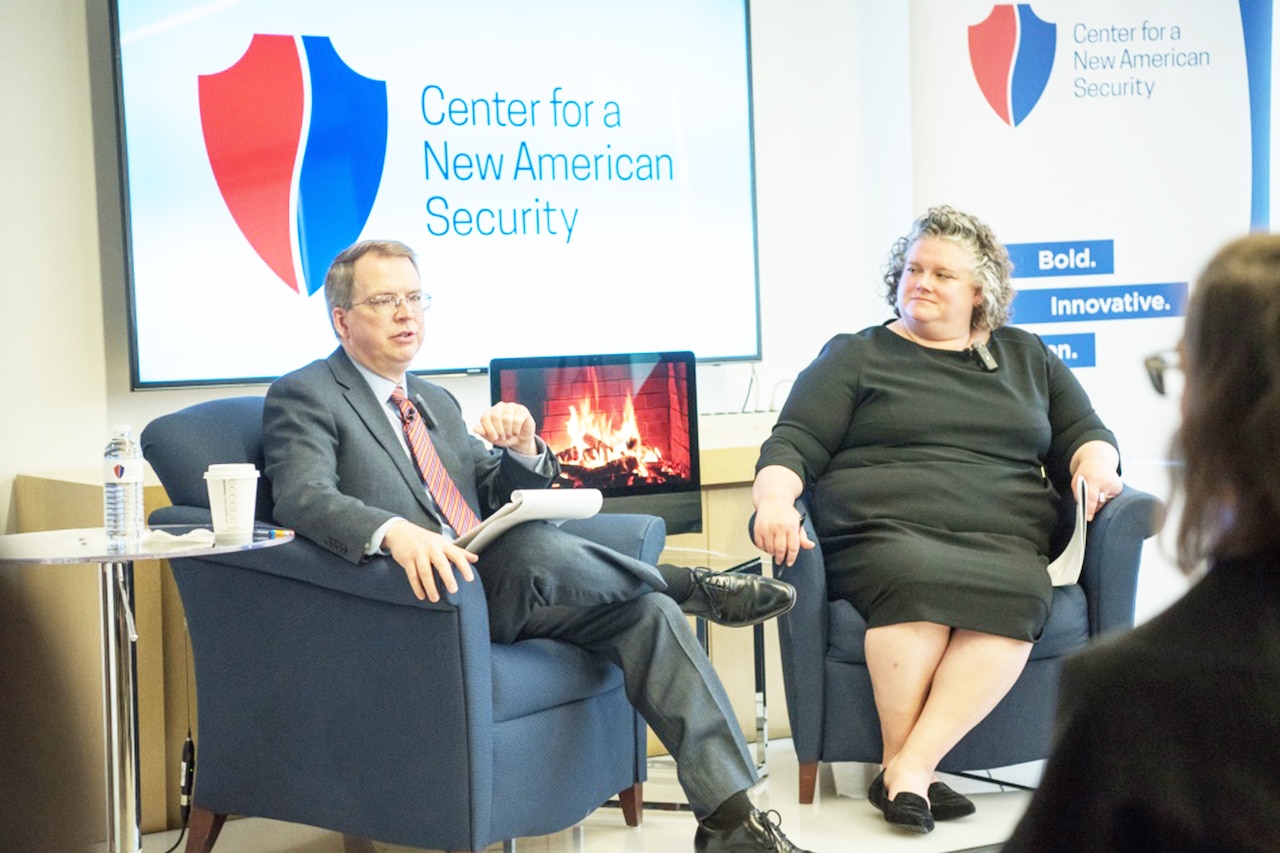Man and woman sit in chairs facing a seminar audience.