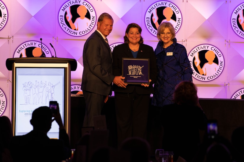 Three people stand holding a plaque.