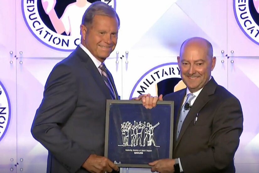 Two men stand holding a plaque