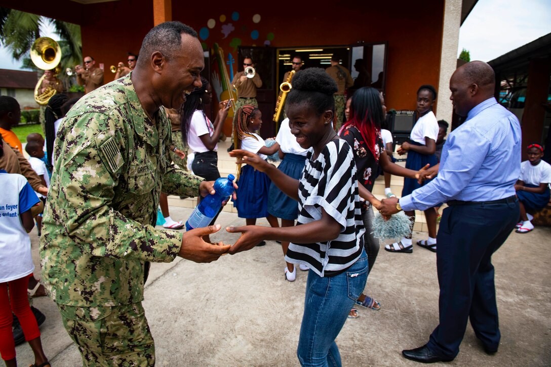 A sailor dances with a woman in the street while a band plays.