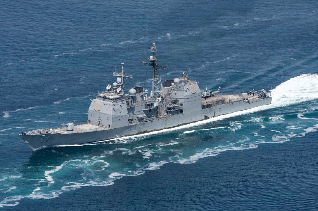 A military ship leaves a white foam wake.