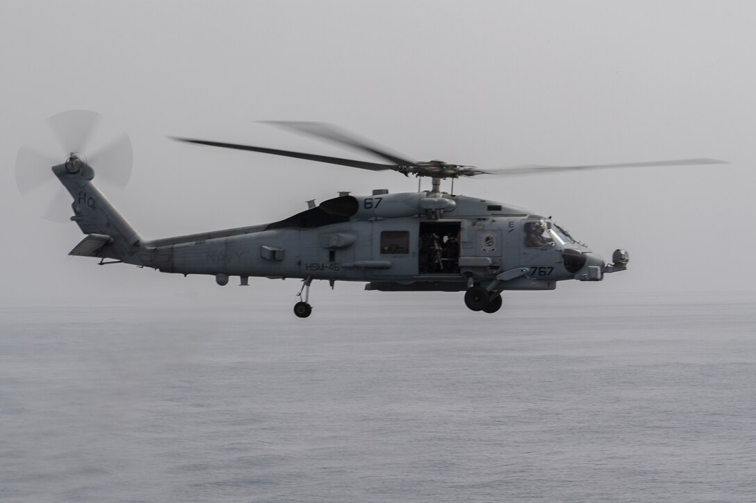 A military helicopter flies over a grey ocean.