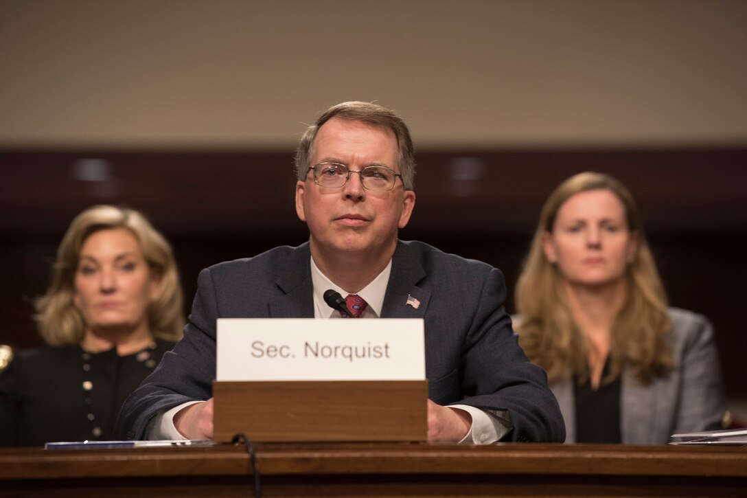 Defense Department Comptroller and Chief Financial Officer David L. Norquist sits at a desk with two people in the background.