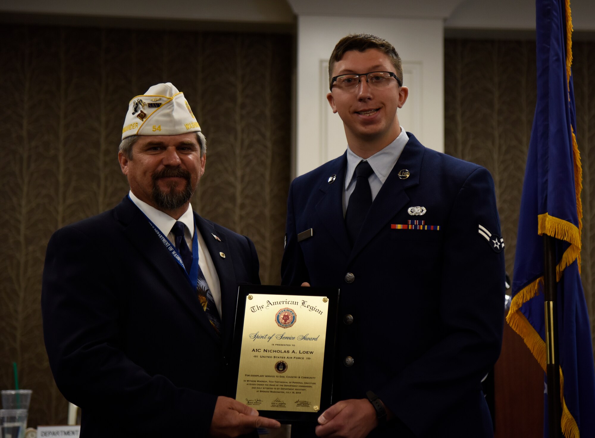 Gary Roach, The American Legion department commander, presents the Spirit of Service Award to Airman 1st Class Nicholas Loew, 92nd Logistics Readiness Squadron fuels distribution operator, during the annual American Legion Department Convention in Spokane, Washington, July 19, 2019. A commitment to the local community led to Loew selflessly volunteering in 33 separate events, for a total of 364 hours. Furthermore, he rallied nineteen volunteers to serve over 3 thousand dinners to less fortunate at the City Gate homeless shelter. (U.S. Air Force photo by Senior Airman Jesenia Landaverde)