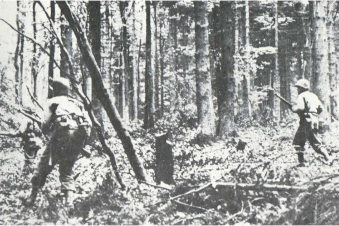 Two World War II soldiers head deeper into woods.