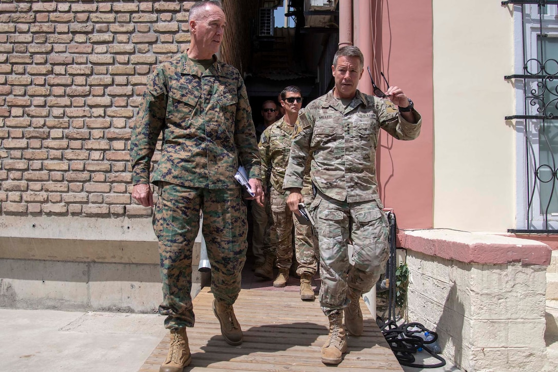Two generals in camouflage uniforms talk while walking.