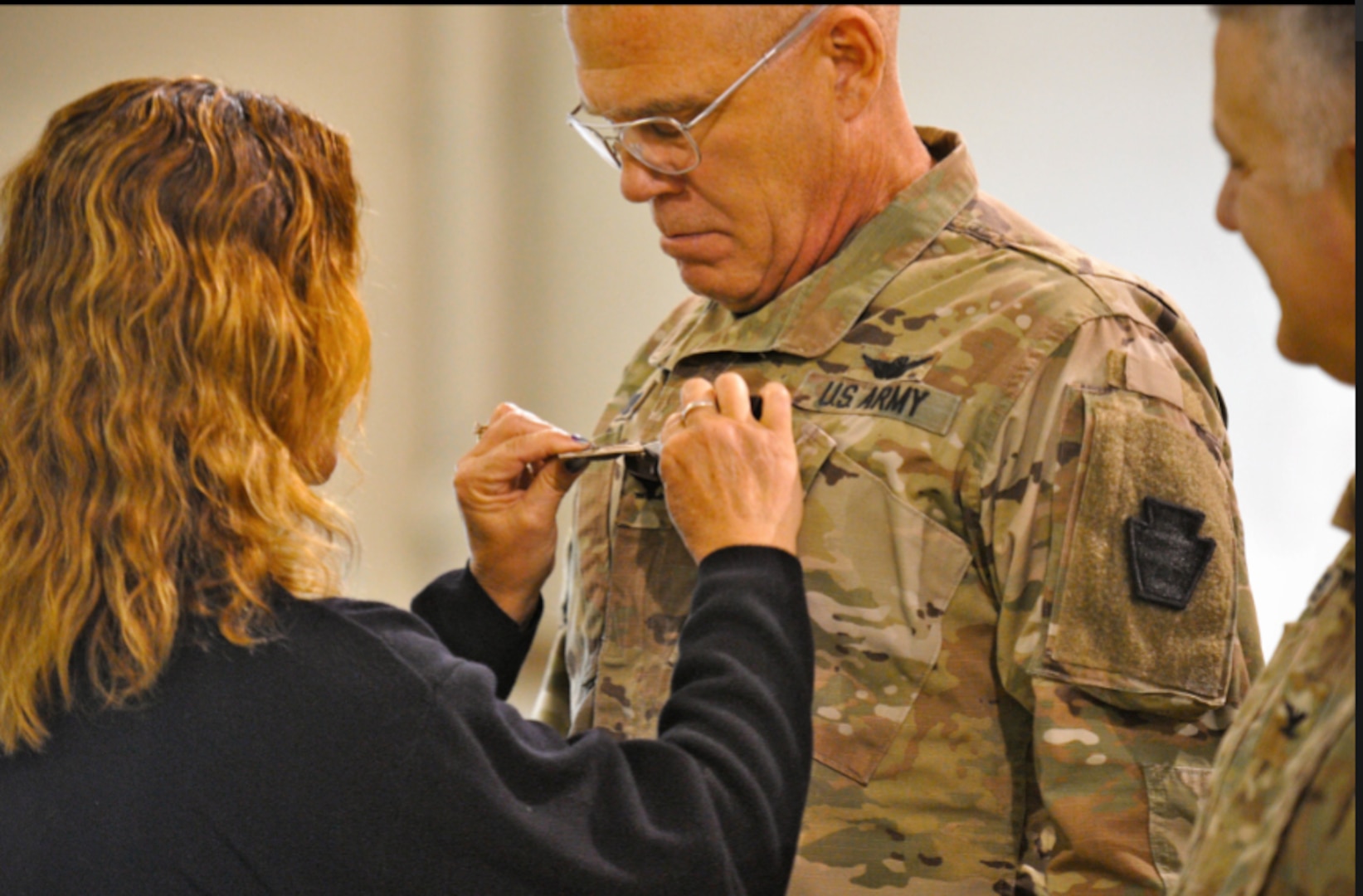 Army Col. Howard Lloyd, right, commander of the 28th Expeditionary Combat Aviation Brigade, has his rank insignia pinned to his uniform by his wife